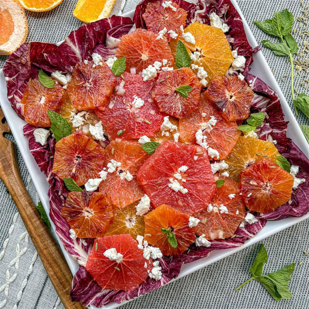 Salad with blood oranges, feta cheese, and mint leaves on a white plate.